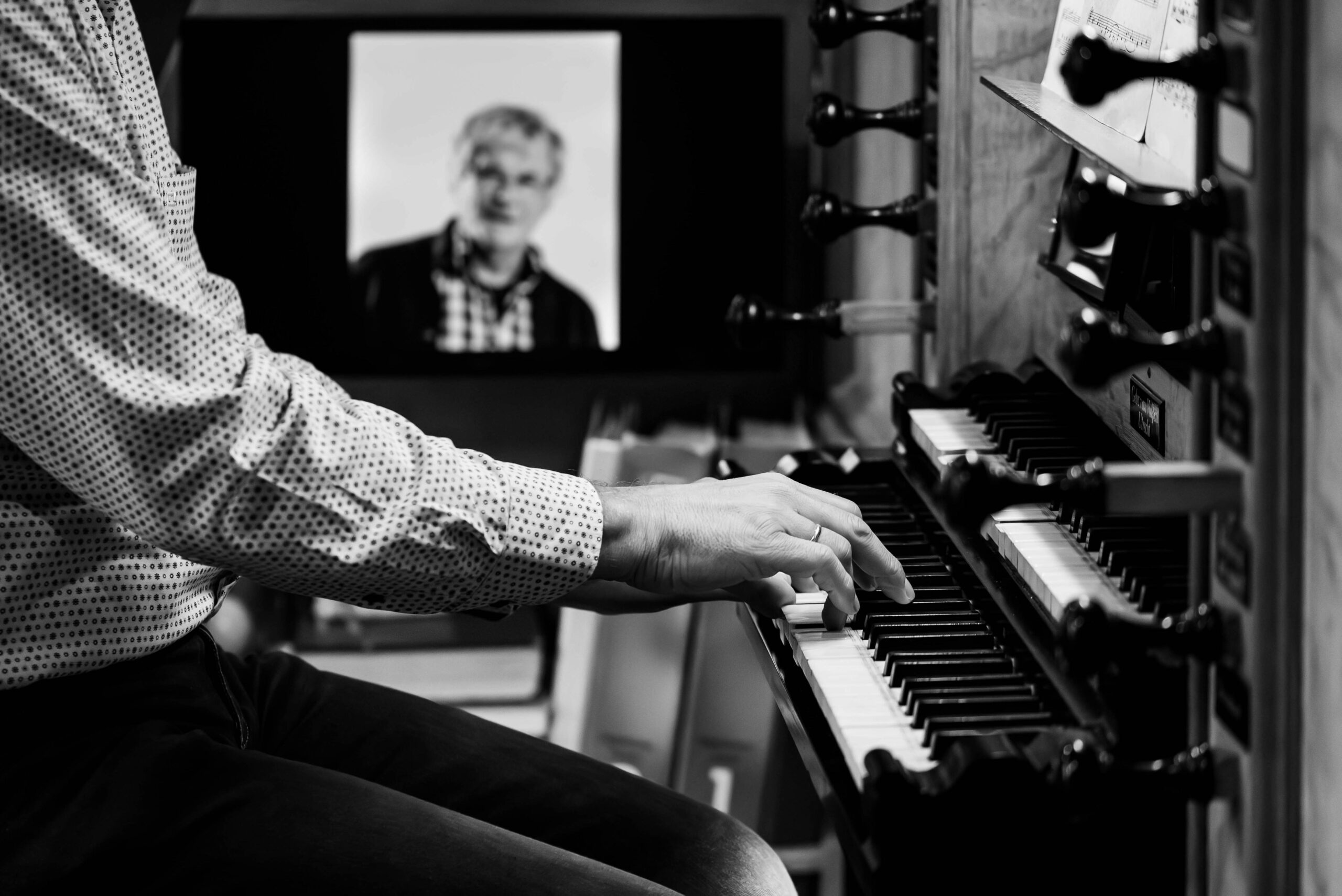 De handen van de organist op het orgel met een foto op de achtergrond.